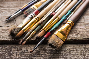 close up view of old paintbrushes on wooden brown surface