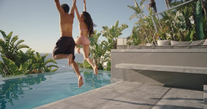 fun couple jumping in swimming pool splashing having fun romantic summer vacation on honeymoon at luxury hotel resort with beautiful ocean view at sunset 4k 