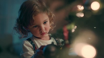 happy little girl decorating christmas tree with beautiful ornaments and baubles enjoying festive decorations at home on calm winter evening 4k footage - Powered by Adobe
