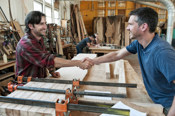 Smiling carpenters shaking hands in workshop