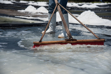 Hombre procesando grandes campos de sal junto con cristales de sal de mar, trabajo muy duro bajo el...