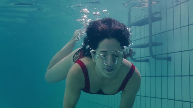 beautiful woman swimming underwater in pool smiling waving hand attractive female enjoying swim in clear water 4k