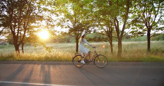 Young beautiful female riding bicycle on countryside road and smiling, feeling happy and relaxed, weekend leisure