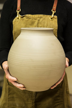 Midsection of potter holding clay pot in workshop