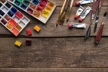 top view of colorful paint palettes and drawing tools on wooden surface with copy space
