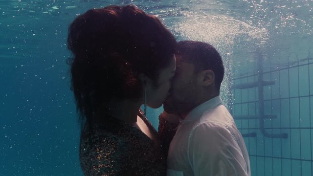 romantic couple kissing underwater in swimming pool wearing clothes young people in love enjoying intimate kiss lovers submerged in water floating with bubbles in passionate intimacy 