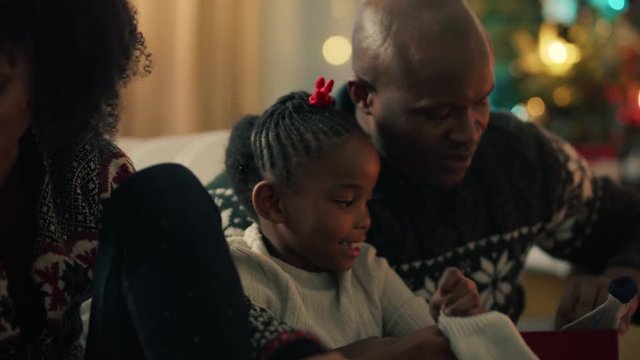 african american family unwrapping christmas presents with children smiling excited little girls enjoying surprise opening gifts mother and father celebrating festive holiday with kids 4k