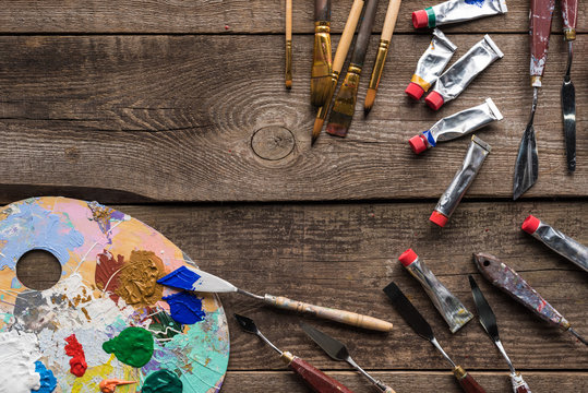 top view of colorful palette with paints and drawing tools on wooden surface with copy space