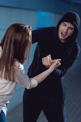 woman defending herself from attacking thief in black hoodie in underpass