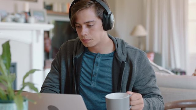teenage boy using laptop computer doing homework bored teen wearing headphones listening to music checking messages on smartphone 4k