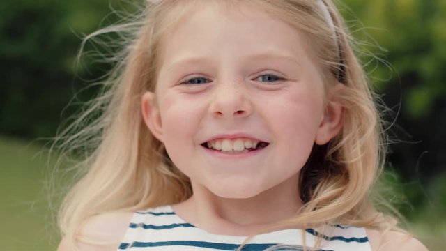 portrait cute little blonde girl smiling with playful excitement looking happy having fun in sunny park outdoors enjoying childhood testimonial concept 4k footage