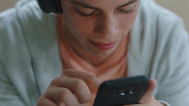 teenage boy texting using smartphone listening to music wearing headphones relaxing on sofa browsing online playing mobile games enjoying sharing messages on social media 4k