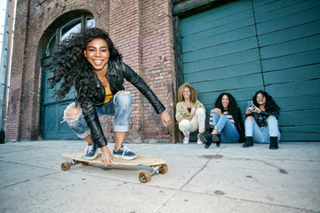 Women looking at their friend skateboarding on sidewalk