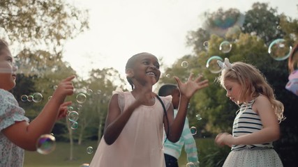 happy little girls playing with soap bubbles blowing in park children having fun summer day friends playing bubble popping game outdoors enjoying childhood freedom 4k - Powered by Adobe