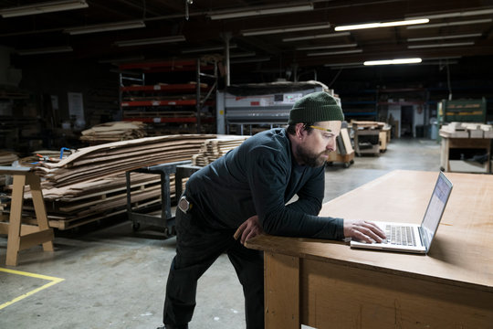 Side view of carpenter working on laptop in workshop - Powered by Adobe
