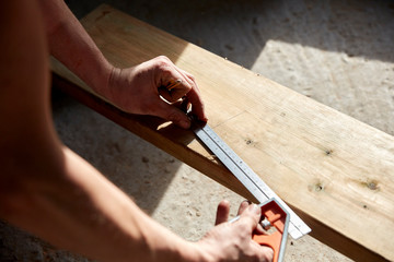 Carpenter measuring plank of wood with metal ruler