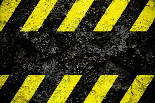 Warning danger sign yellow and black stripes pattern with black area over concrete cement wall facade peeling cracked paint. Background design for do not enter the area, caution, danger, hazard.
