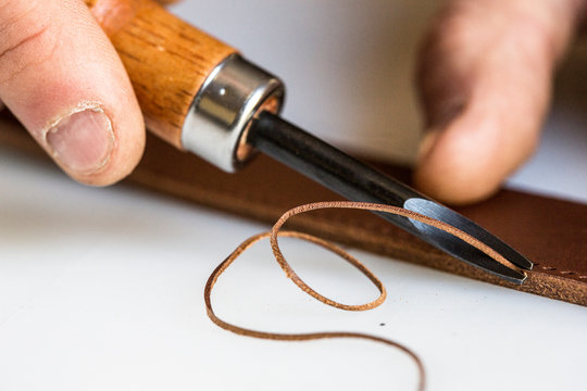 Close up of craftsman using forked cutter on leather strap