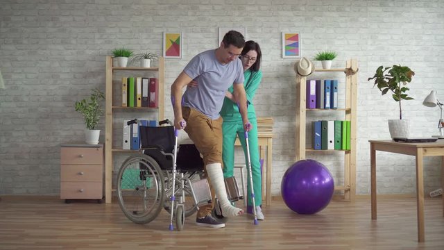 doctor helps a man get up with a leg injury from a wheelchair after an injury