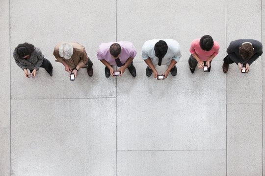 Overhead view of business people standing in row and using smartphone in office