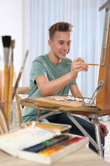 Fototapeta na wymiar Teenage boy painting on easel in workshop. Hobby club