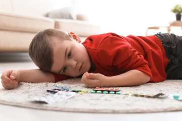 Obraz na płótnie Canvas Little child with pills lying on floor at home. Household danger