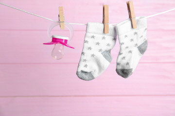 Pair of socks and pacifier on laundry line against pink wooden background. Baby accessories