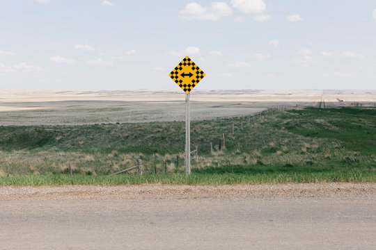View of arrow intersection sign on rural farmland