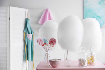 Tasty cotton candy and other sweets on table in room. Space for text