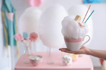 Fototapeta na wymiar Woman holding cup with cotton candy dessert on blurred background, closeup. Space for text