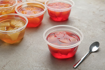 Plastic containers with tasty jelly desserts and spoon on grey table