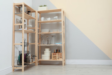 Wooden shelving units with kitchenware near color wall, space for text. Stylish room interior