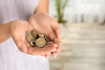Young woman with handful of coins indoors, closeup view. Space for text