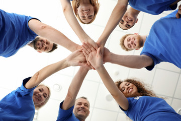 Team of volunteers putting their hands together on light background, bottom view