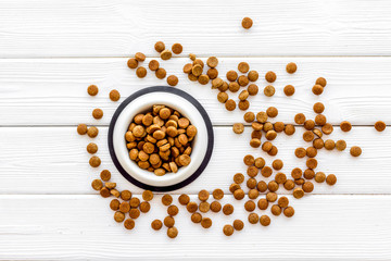 Dry pet food in bowl on white wooden background top view
