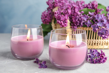 Burning wax candles in glass holders and lilac flowers on grey table