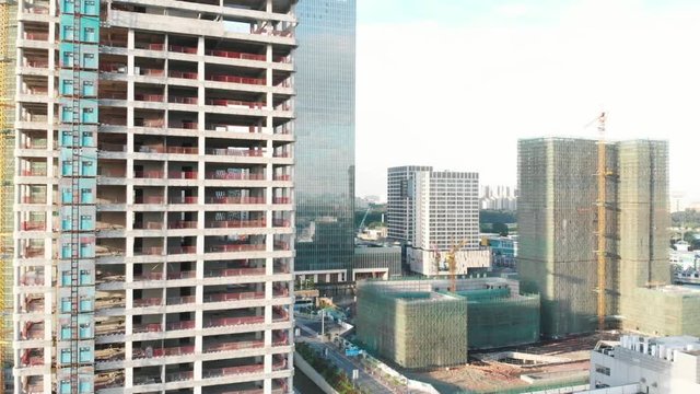 Video from the air. The drone flew sideways, in the frame we see the high-rise frames, construction cranes. In the background are already finished glass skyscrapers. Long shadows from the rising sun.