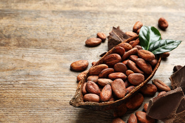 Pod with cocoa beans and chocolate pieces on wooden table, space for text