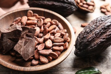 Bowl of cocoa beans and chocolate pieces with pods on wooden table, closeup