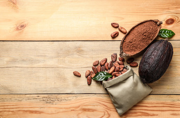Flat lay composition with cocoa pods and bag of beans on wooden table, space for text