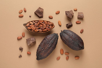 Cocoa pods with beans and chocolate pieces on light brown background, flat lay