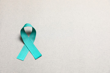 Teal awareness ribbon on grey paper, above view with space for text. Symbol of social and medical...
