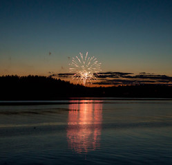 A firework explodes in the distance reflecting orange and red into the water. 