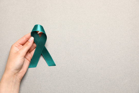 Woman holding teal awareness ribbon on grey paper, top view with space for text. Symbol of social and medical issues - Powered by Adobe