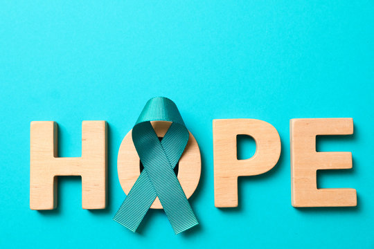 Word Hope made of wooden letters and teal awareness ribbon on light blue background. Symbol of social and medical issues