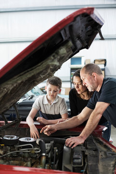 Multigenerational family repairing car in automobile repair shop