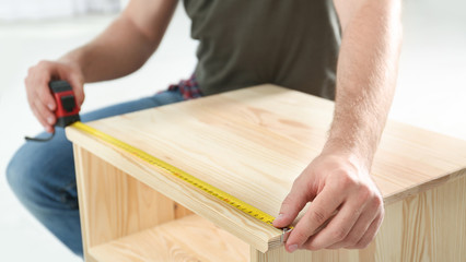 Young working man using measure tape at home, closeup
