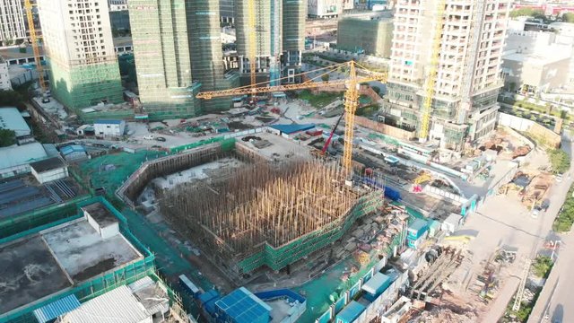 The camera smoothly lowers. The focus is on the construction crane, the pit for a new skyscraper. Long shadows from the rising sun. Guangzhou, China