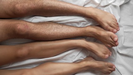 Top view. Male and female legs closeup in bed on a white sheet. The feet move in time to the left and to the right synchronously.