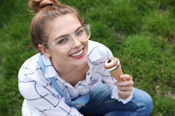 Young happy woman with ice cream cone sitting on grass in park